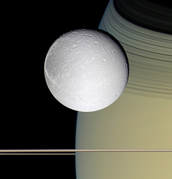 Dione vznášející se nad povrchem planety Saturn